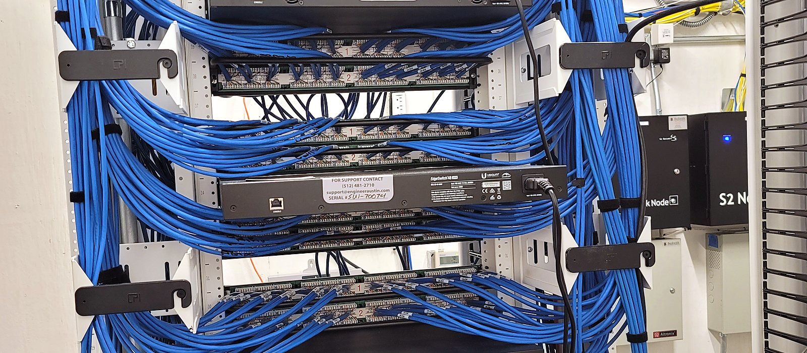 Blue Category 6 cabling dressed through vertical managers into patch panels and switches on an open rack, installed by Engineer Austin