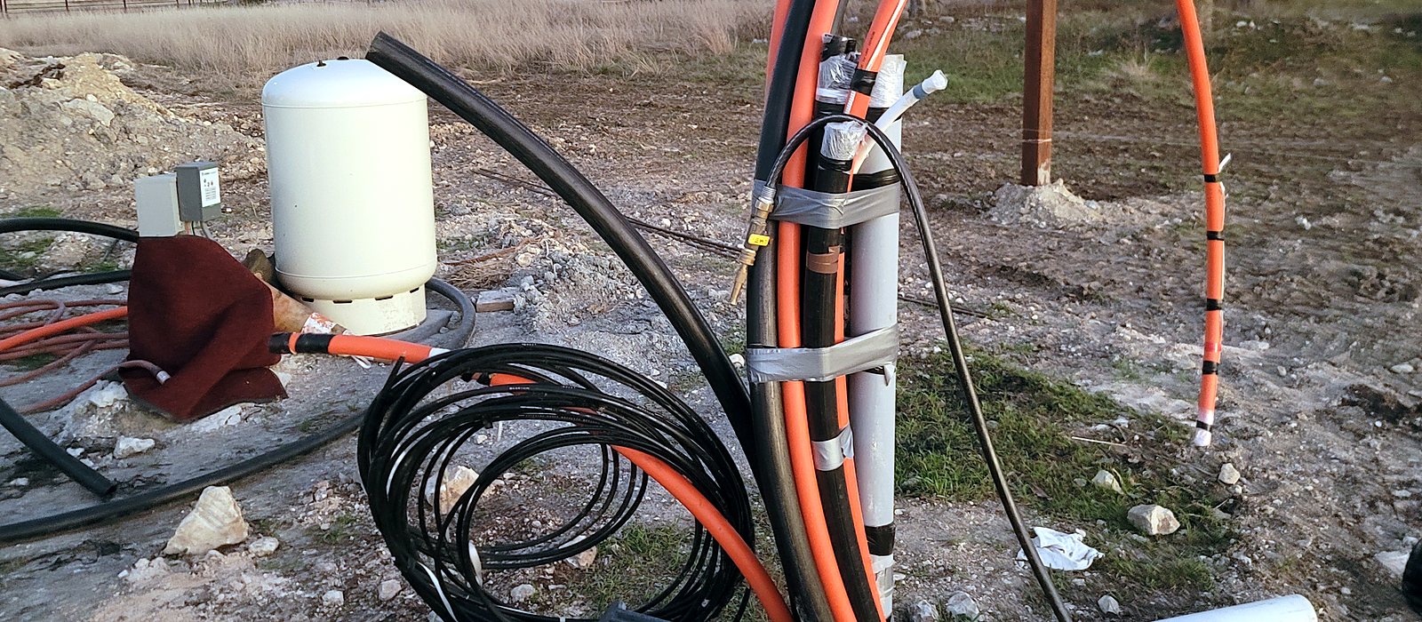 Orange fiber innerduct and conduit rising from the ground at a rural site during an Engineer Austin fiber build