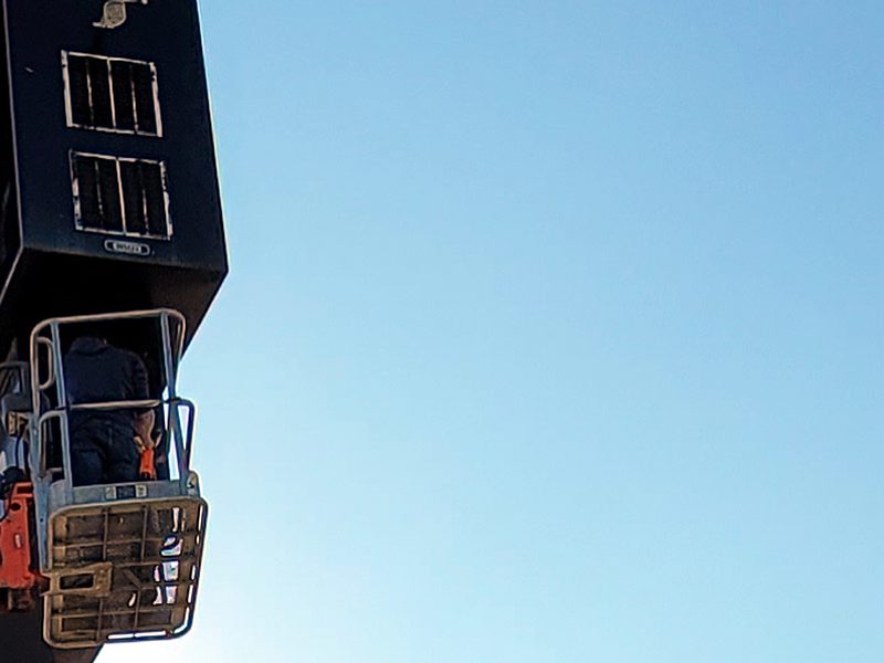 Engineer Austin technician in a lift basket at the open cabinet of a tall pylon sign, repairing the fiber that feeds it