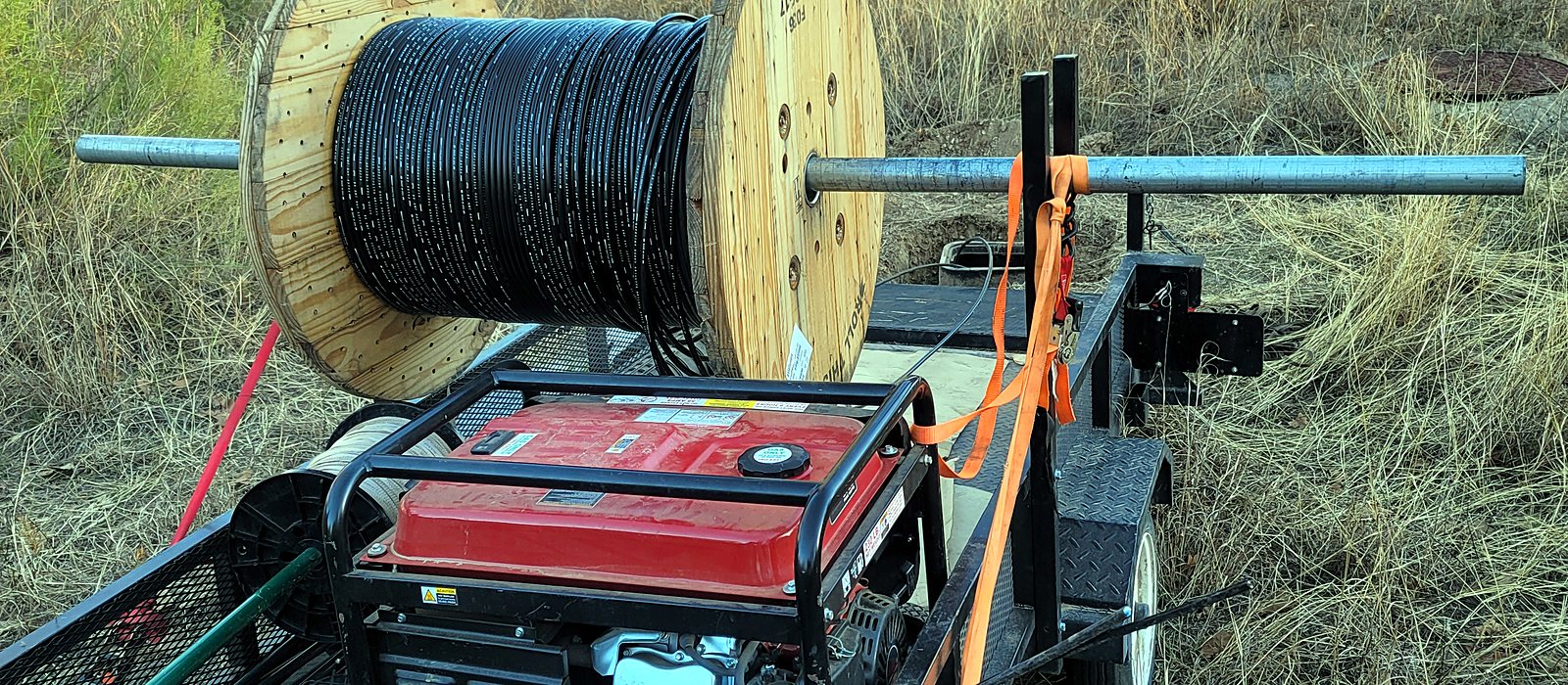 Engineer Austin cable trailer with a reel of outdoor cable and a generator, staged in a field for an outside-plant build