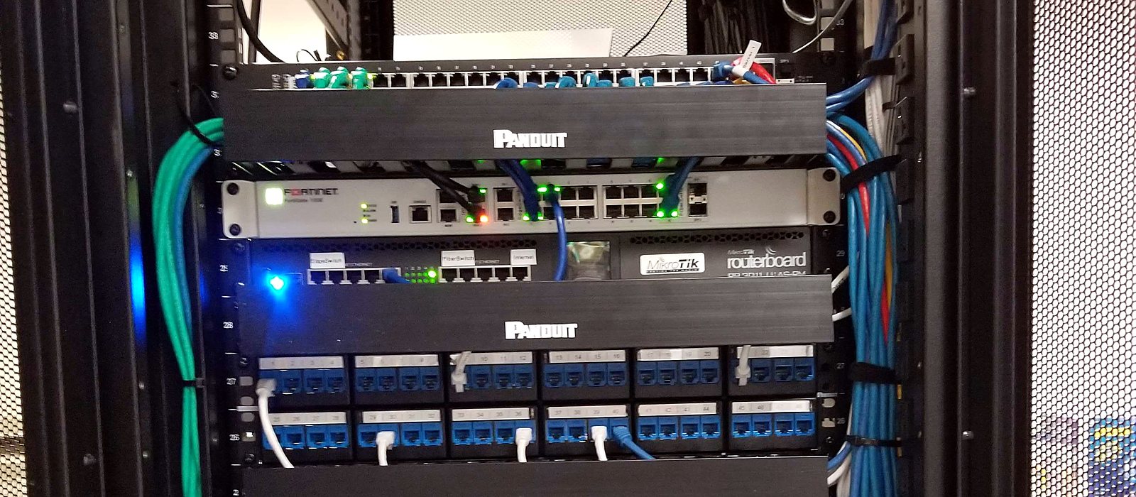 Network cabinet with a FortiGate firewall, a MikroTik router and patch panels with cable management, installed by Engineer Austin