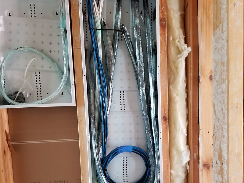 Bundled cable runs coiled into a structured-media enclosure between wall studs, before drywall