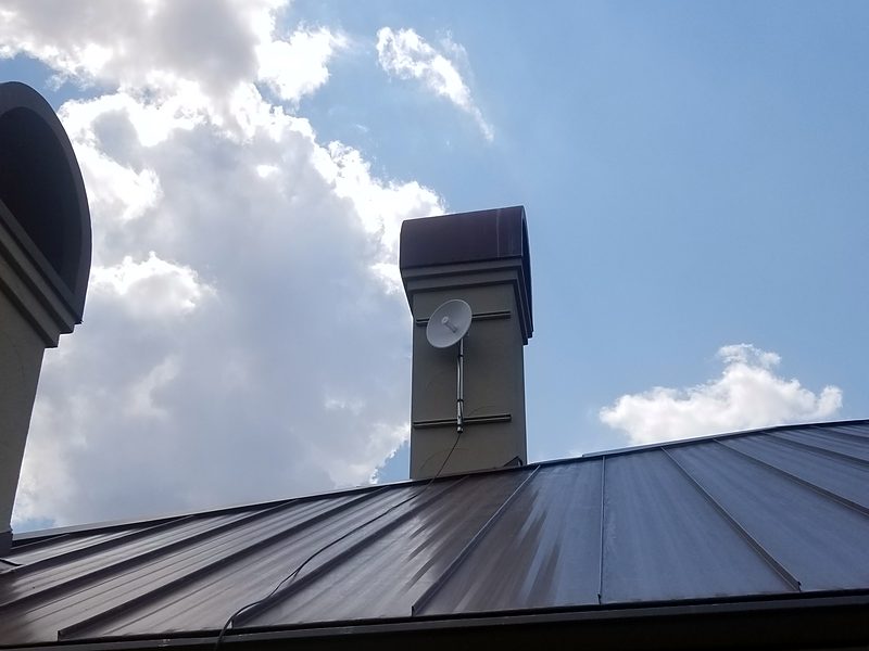 Point-to-point dish bracketed to a chimney above a standing-seam metal roof
