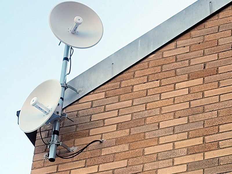 Two point-to-point dishes stacked on a wall-offset mast at the corner of a brick building