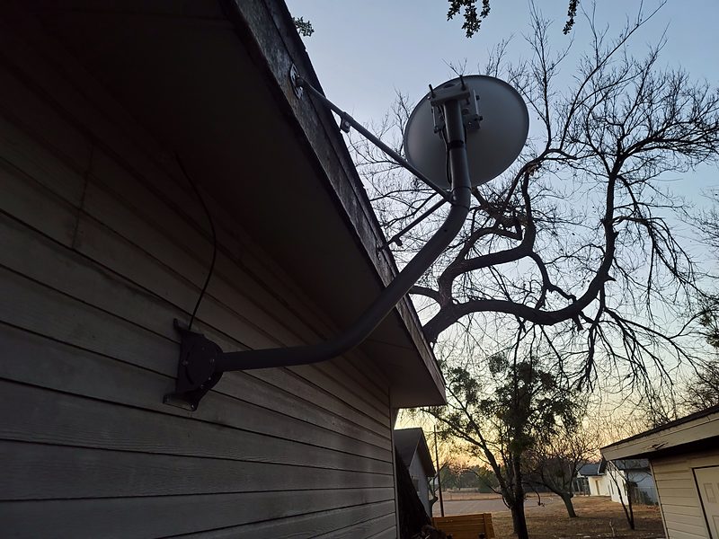 Dish on a curved wall arm on lap siding, against a sunset sky