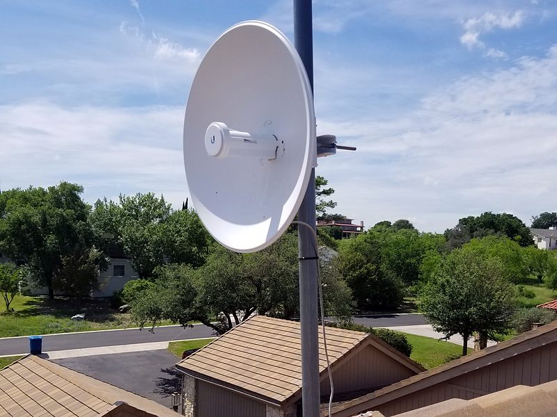 Dish on a mast clamped to a roof gable above a tile roof