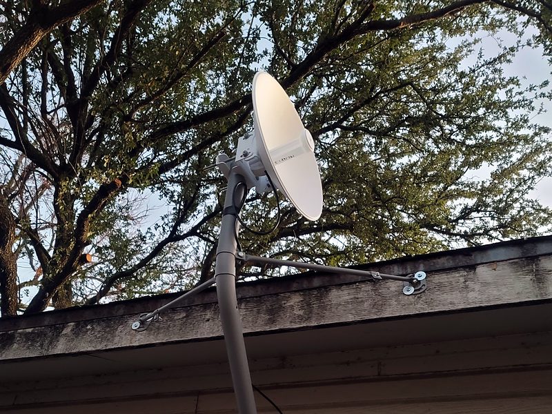 Dish on a J-arm mount with stay braces, rising above a roof edge