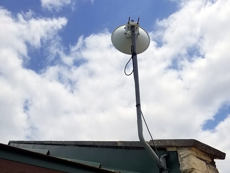 Dish on an offset pipe mount above a stone wall and metal roof