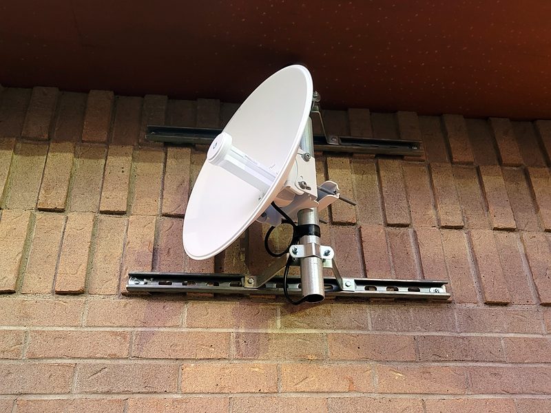 Dish on a strut-channel mount fixed to a brick wall under a tile eave