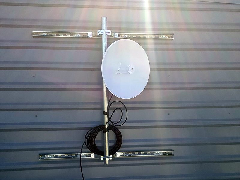 Dish on a strut-channel wall mount on metal siding with a neat cable service loop