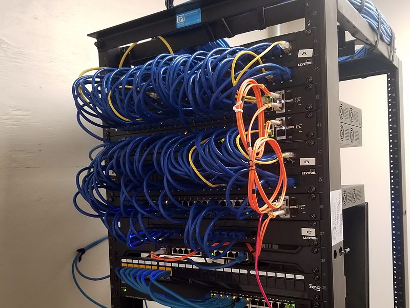 Open rack with dozens of blue patch cords and orange fiber jumpers neatly bundled