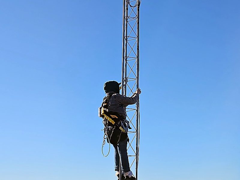 Climber in a full-body harness ascending a lattice tower