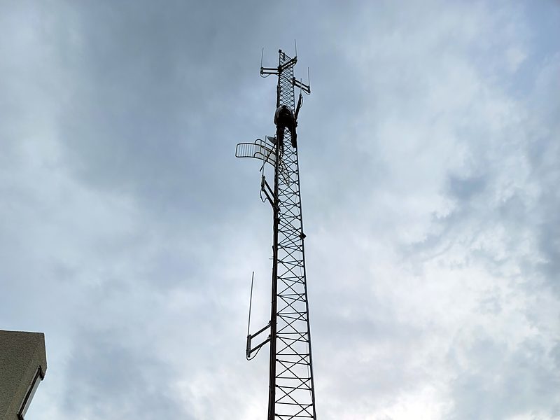 Engineer Austin climber working among the antennas at the top of a self-supporting lattice tower under a stormy evening sky