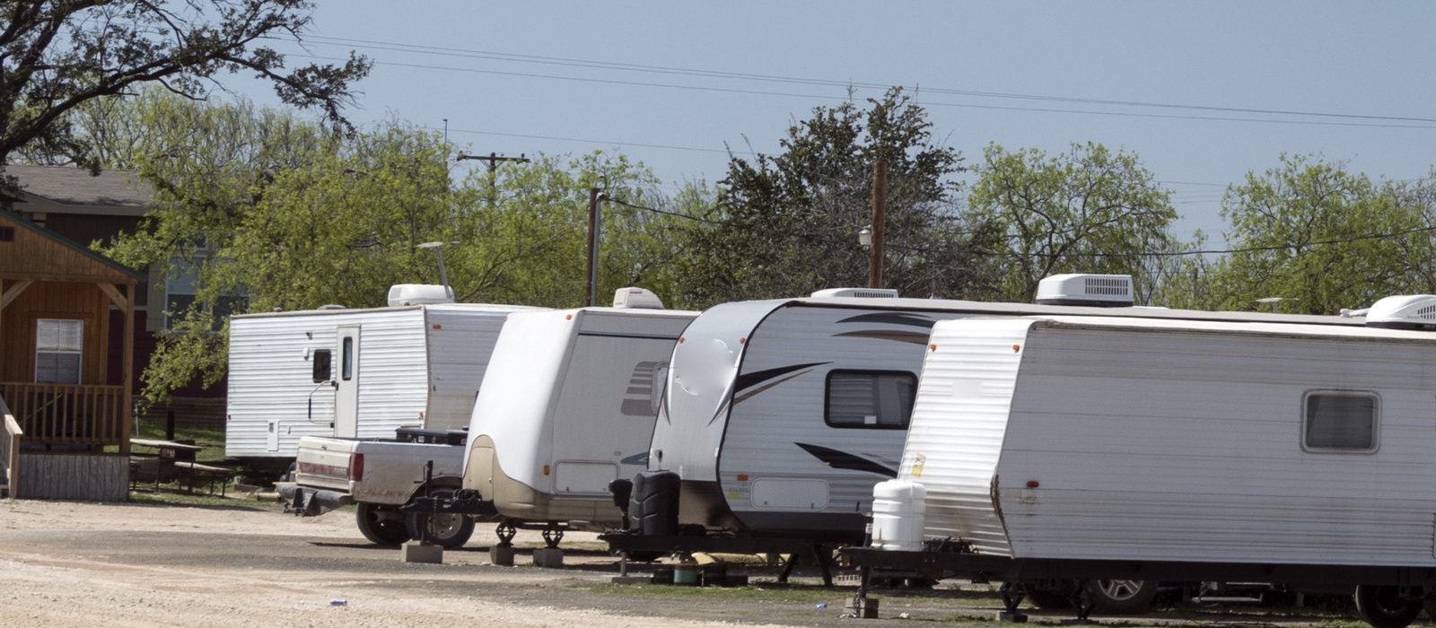 Row of travel trailers parked on gravel pads under live oaks at a small Texas RV park